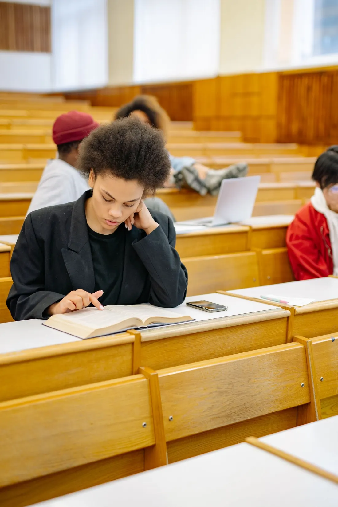 A student reading a textbook at a desk in a university lecture hall